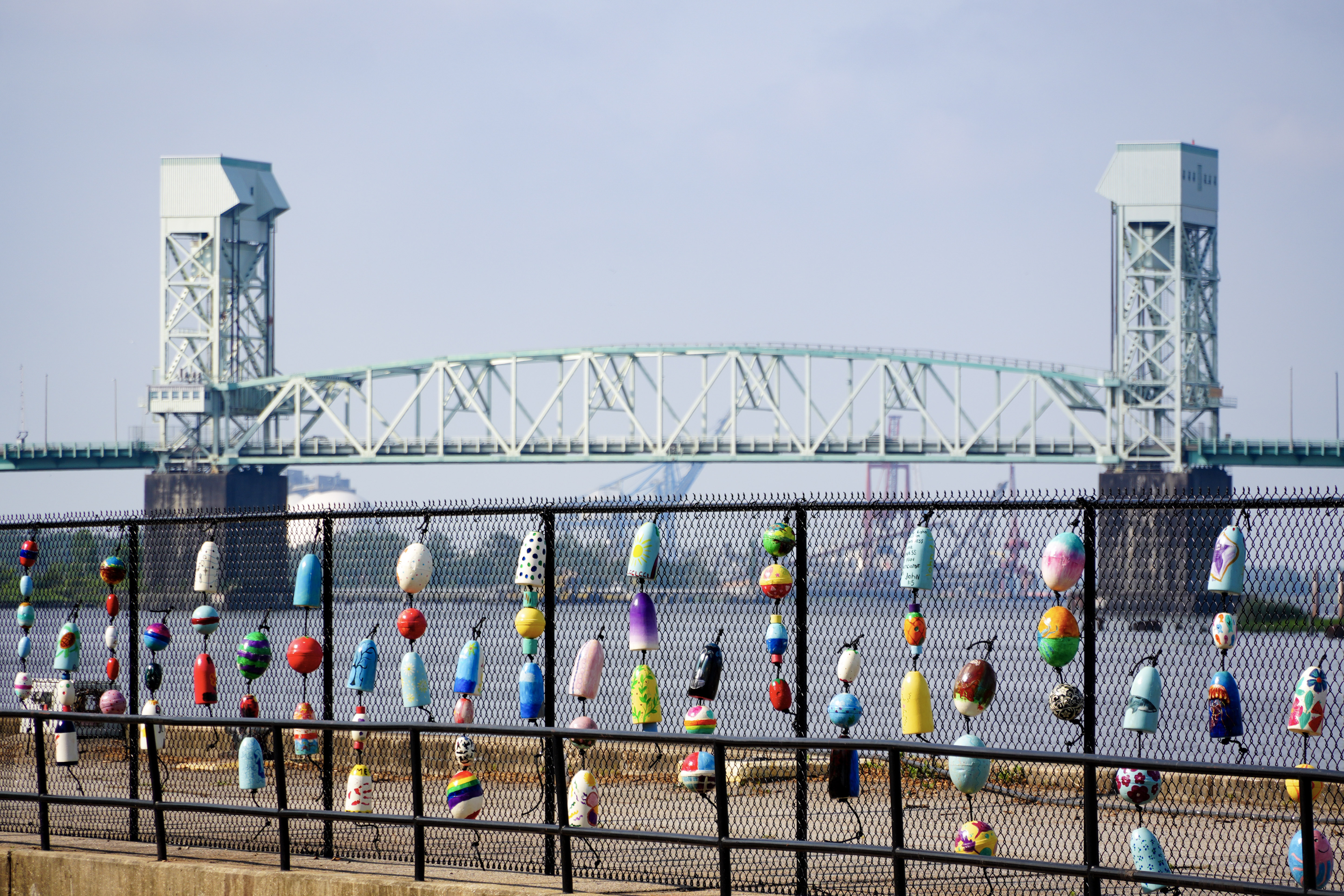 Painted buoys hanging on a fence in front of a bridge